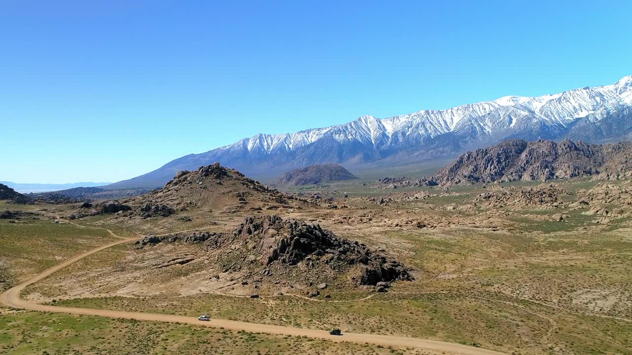 空中倾斜向下拍摄的车辆在土路上移动的岩层，无人机飞越景观在阳光明媚的日子-主教，加州视频素材