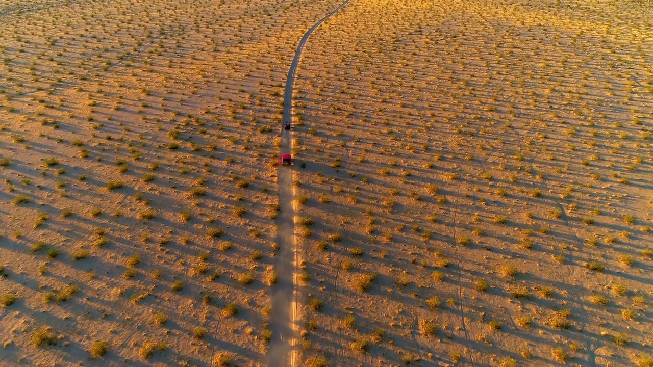 空中倾斜拍摄的车辆在泥泞的道路在灌木丛中，无人机在日落飞越沙漠-莫哈维沙漠，加利福尼亚州视频素材