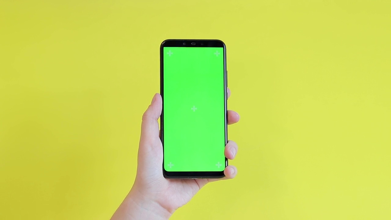 一位女士拿着黄色背景上绿色空白屏幕的智能手机视频素材