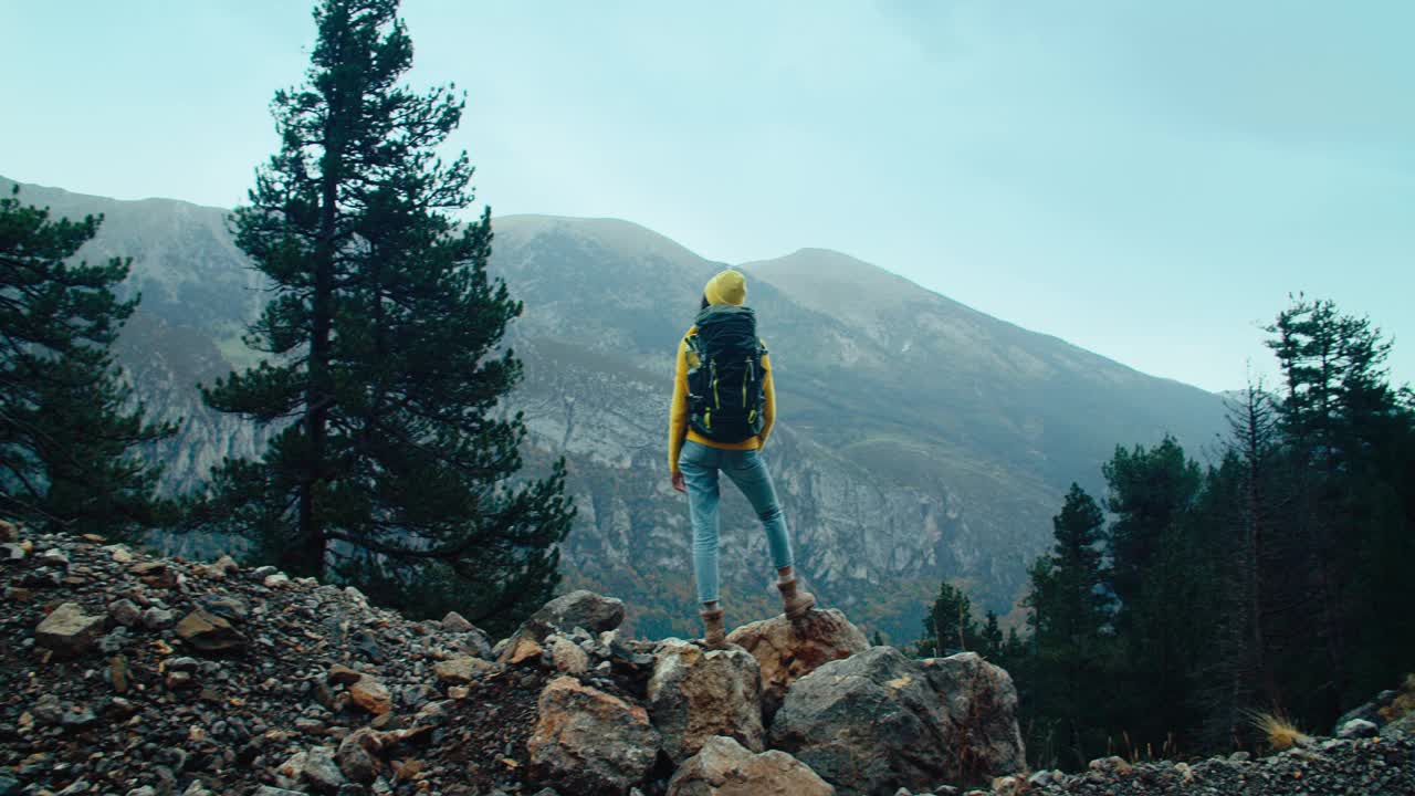 女徒步旅行者背着背包站在山边视频下载