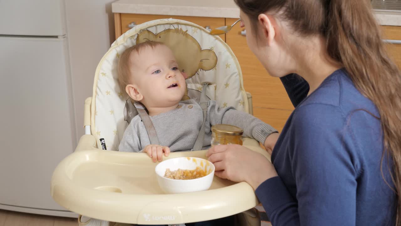 快乐的小男孩张开嘴要舀粥。育儿理念，健康营养和婴儿护理视频素材