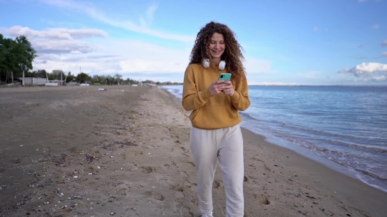 一名年轻女子在希腊海滩边走边玩手机视频素材