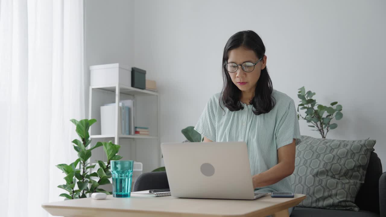 亚洲女人用笔记本电脑，在家打公司报告视频素材