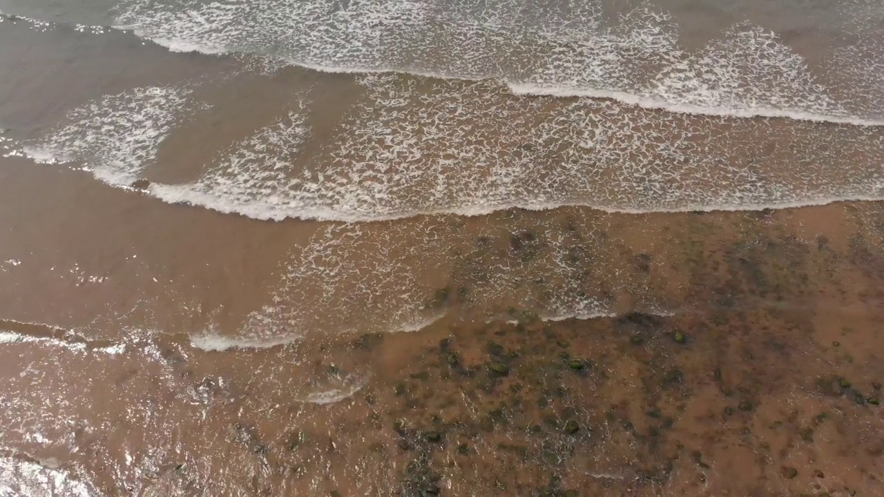 无人机拍摄的海浪冲击海岸线棕色沙滩的画面视频素材