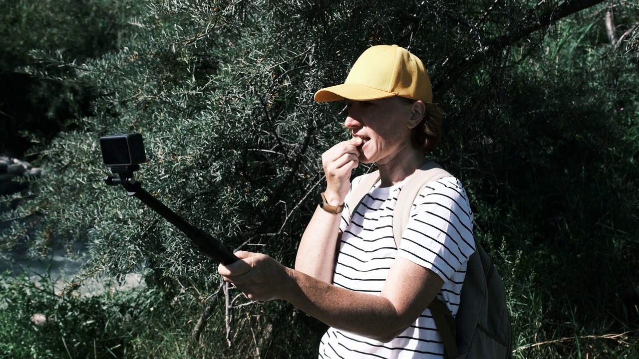 一位成熟的女性游客在小山城的河岸边品尝沙棘果视频下载