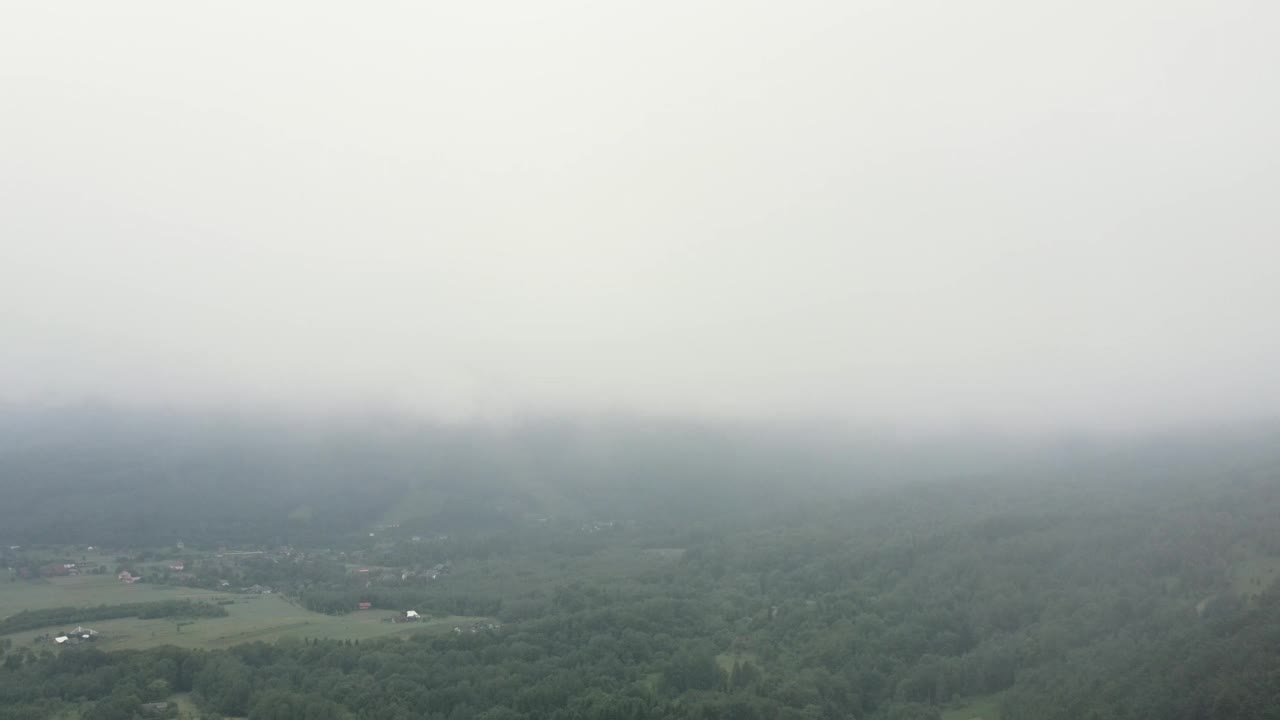 在多云的夏日，云雾笼罩的山村，美丽的绿色大田野和小房子，从无人机上看到的晨雾渐渐消散。乡村景观概念视频素材