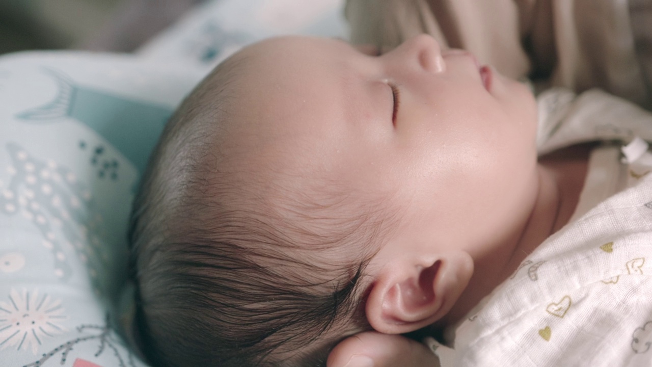 熟睡的亚洲新生婴儿的脸部特写。在妈妈的怀抱里有一个开朗、可爱的心情。视频下载