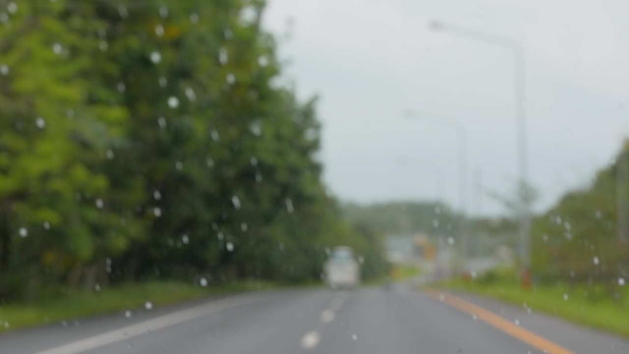 在雨天的旅行中，从行驶的汽车透过挡风玻璃看到的模糊景象。视频下载