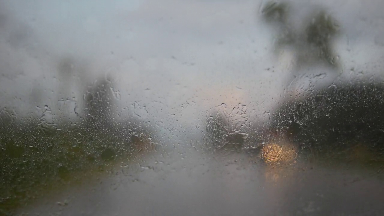 从行驶中的汽车透过雨刷在大雨中运转的挡风玻璃看到的景象。视频素材