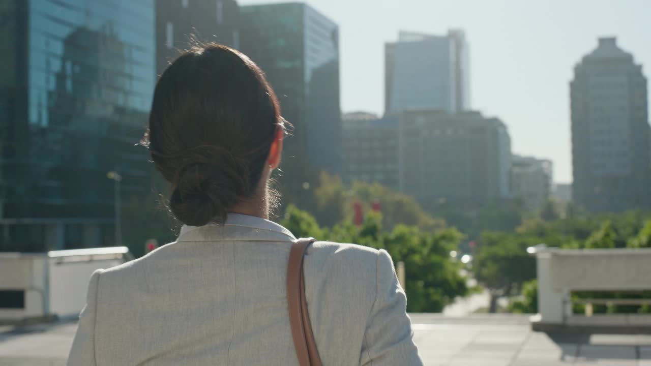 商业女性，在城市中散步，寻找机会，成功和愿景。背后是一个职业女性或员工，有光明的未来，城市建筑和雄心勃勃的旅行视频素材