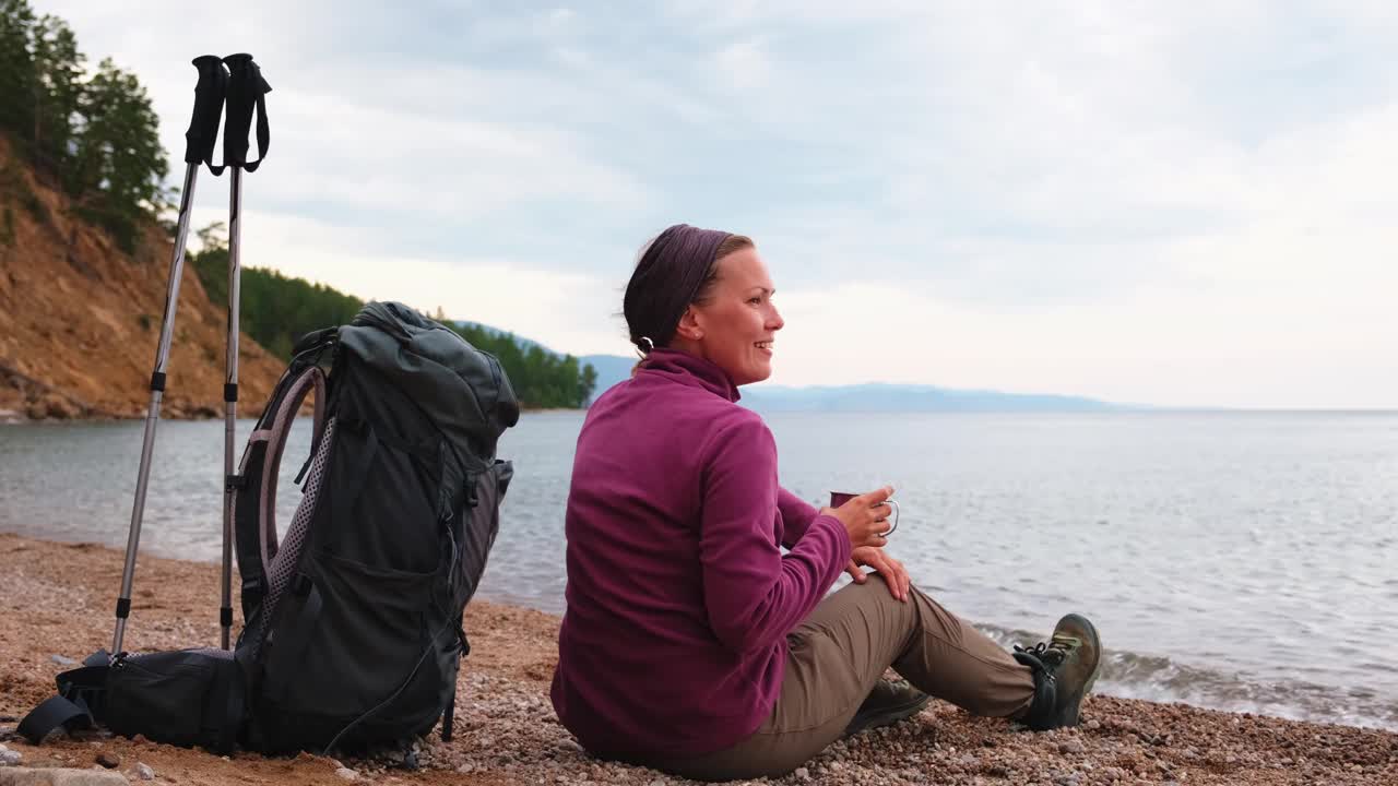 徒步旅游探险。徒步旅行后休息的背包客女人看着美丽的景色。徒步旅行的女孩，背着背包的女游客坐在湖边。徒步旅行的女人享受徒步旅游积极的假期。视频素材