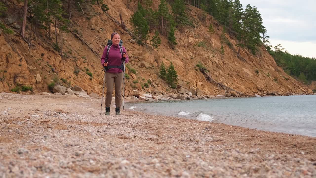 徒步旅游探险。徒步旅行者，女孩，女游客背着背包在湖边散步。背包客徒步旅行的女人享受美丽的海滩景色。年轻快乐的女人享受徒步旅行旅游积极的假期。视频素材