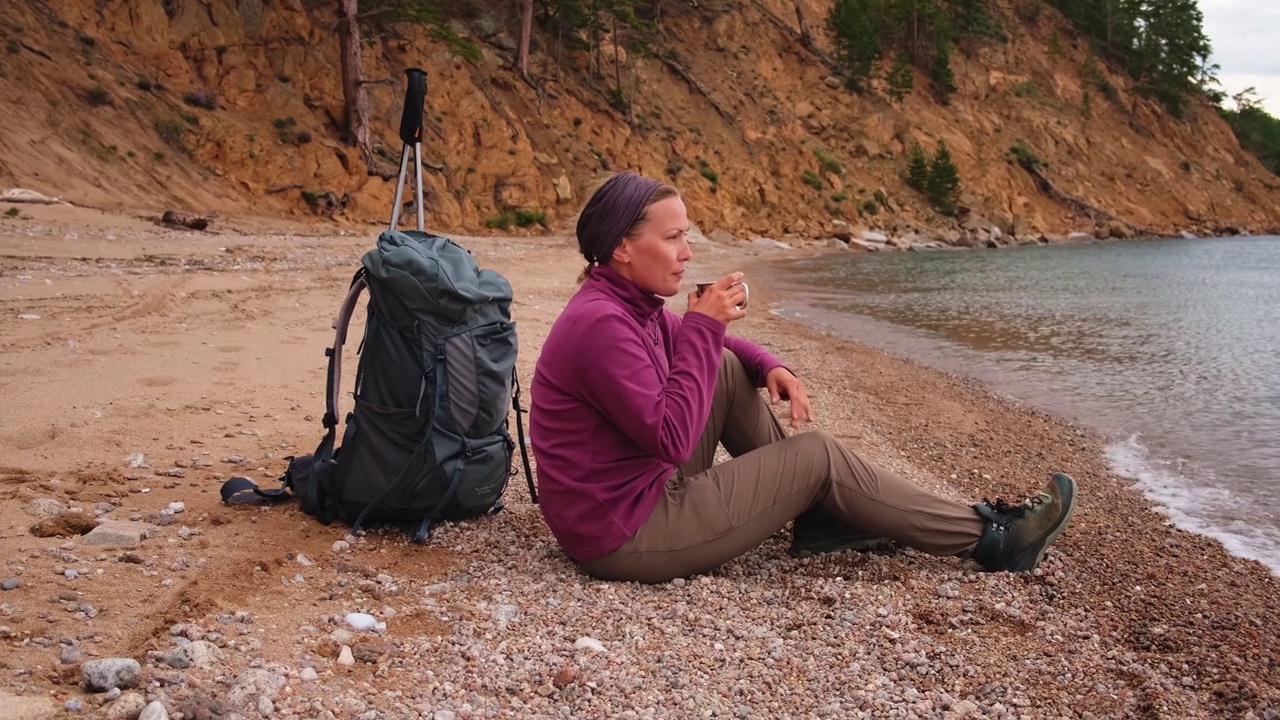 徒步旅游探险。徒步旅行后休息的背包客女人看着美丽的景色。徒步旅行的女孩，背着背包的女游客坐在湖边。徒步旅行的女人享受徒步旅游积极的假期。视频素材