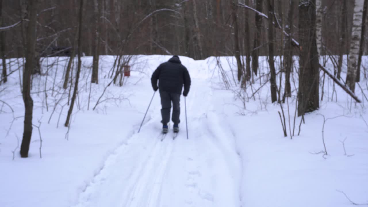 一个50岁的男人冬天在森林里滑雪视频素材