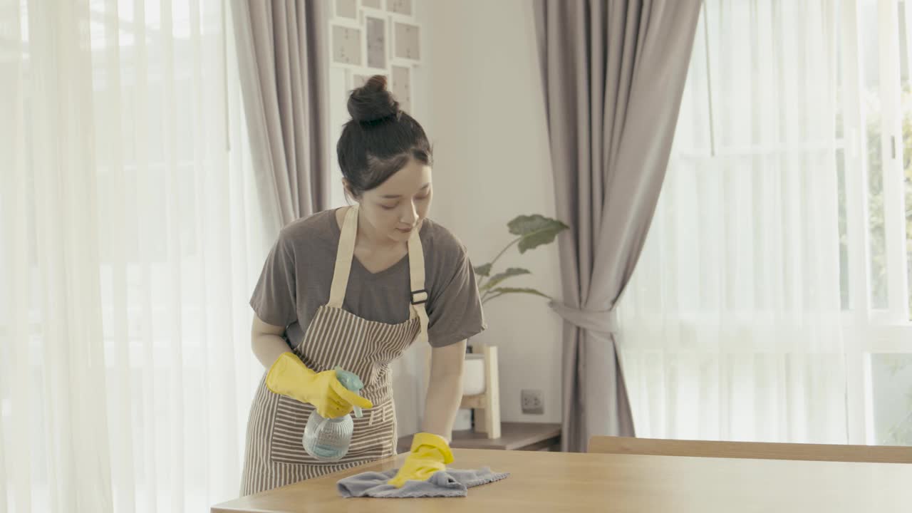 戴着黄色橡胶防护手套的年轻女子正在清洁餐桌表面。使用清洁喷雾的妇女。视频下载