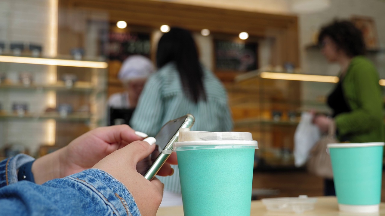 一个女人坐在咖啡店里拿着手机和一杯咖啡的特写。视频素材