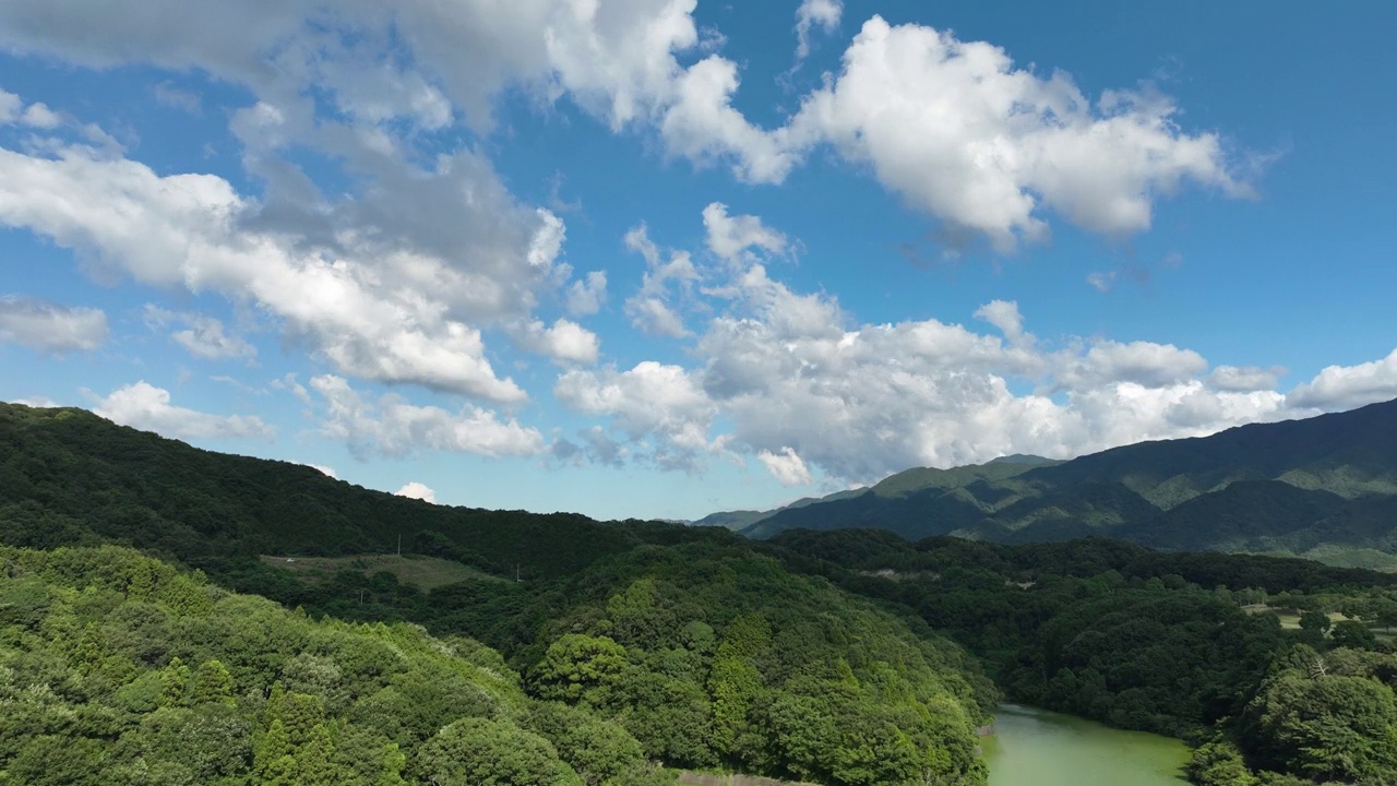 无人机在多云的天空下飞过绿色的森林山丘，时间流逝视频素材