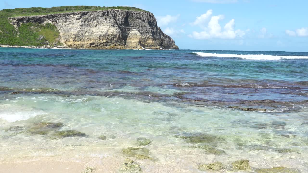 在加勒比海瓜德罗普岛的沿海地区，潮汐带着海浪和远处的岩石悬崖视频下载