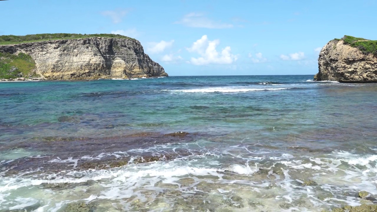 在加勒比海瓜德罗普岛的沿海地区，潮汐带着海浪和远处的岩石悬崖视频素材