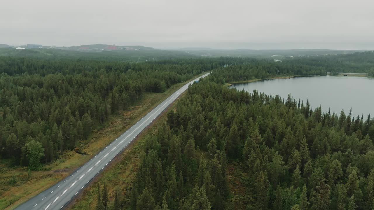 一架无人机直接飞过一辆在森林和湖泊之间的道路上行驶的红色汽车视频素材