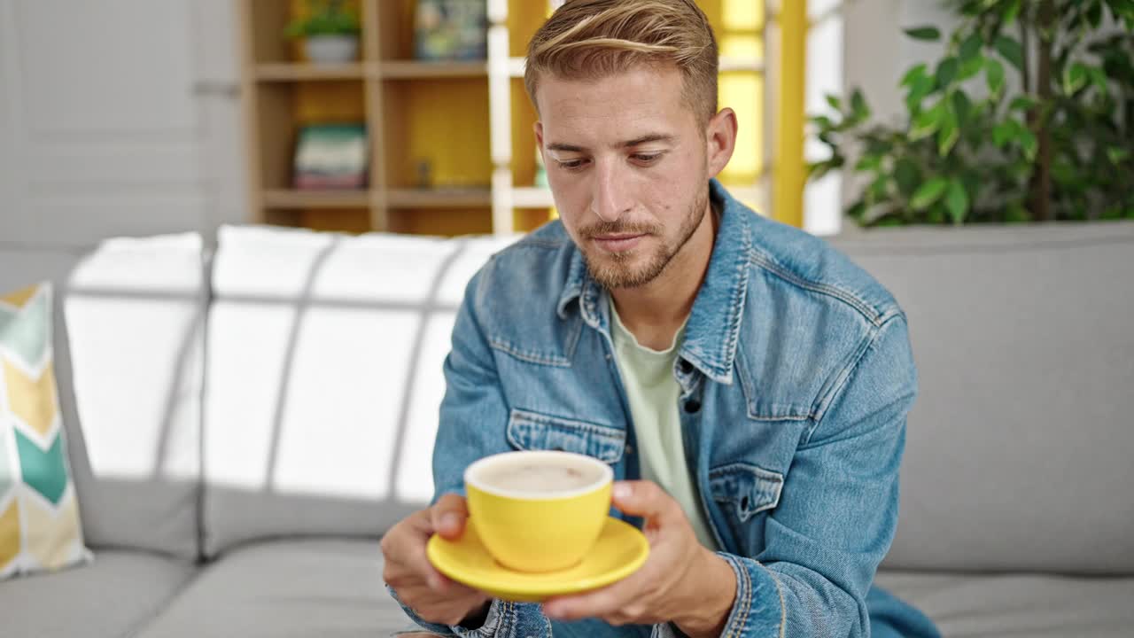 年轻的白人男子捧着一杯咖啡坐在家里的沙发上视频素材