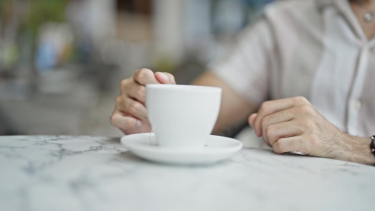 年轻的西班牙裔男子在咖啡店的露台上端着一杯茶视频素材