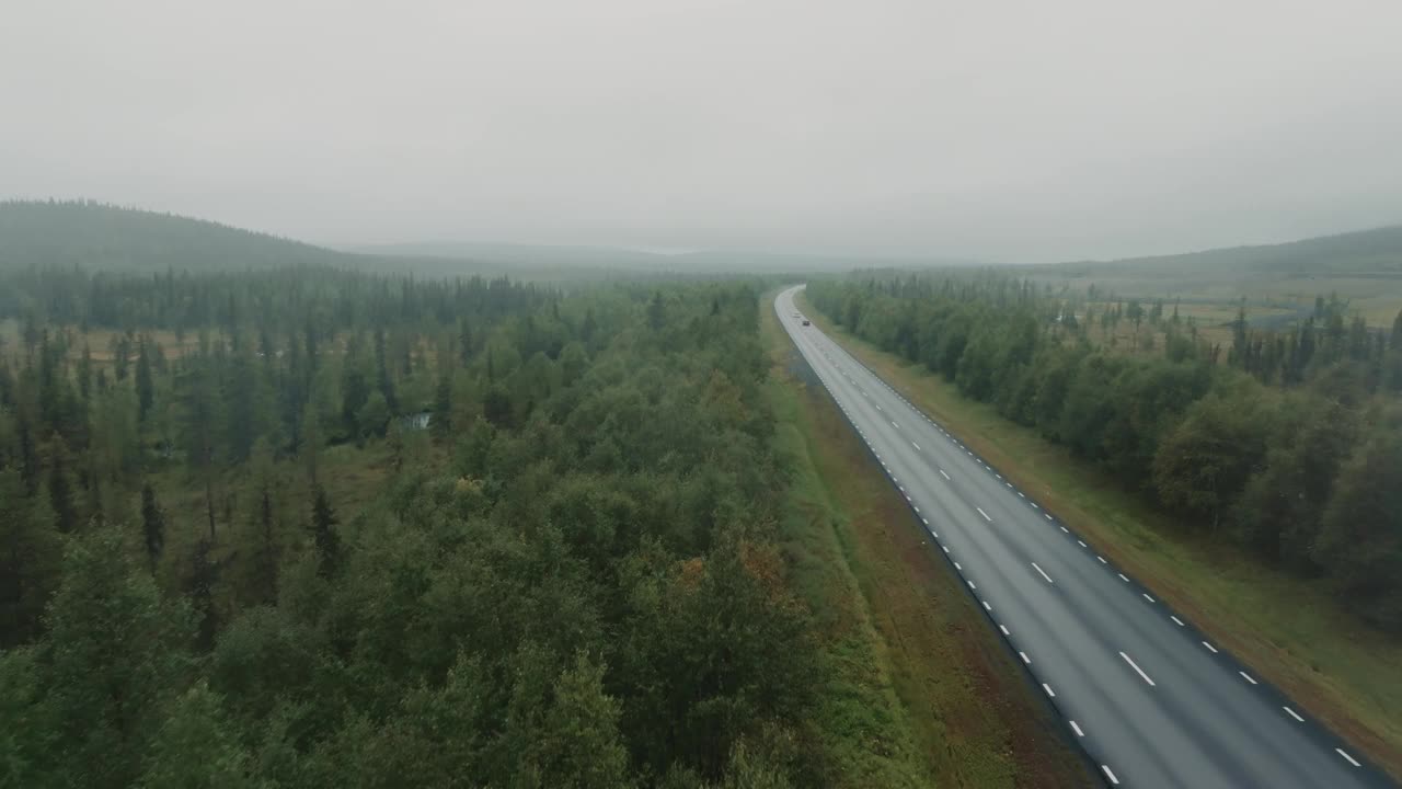 下雨天，无人机跟随红色SUV行驶在野外的道路上。视频素材