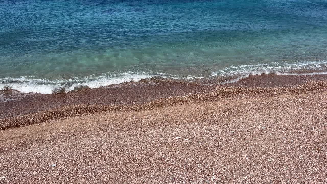 海水清澈，沙滩上有粉红色的鹅卵石和沙子。视频素材