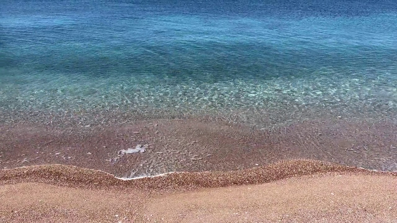 大海上透明的蓝色波浪，沙滩上有鹅卵石和沙子。视频素材