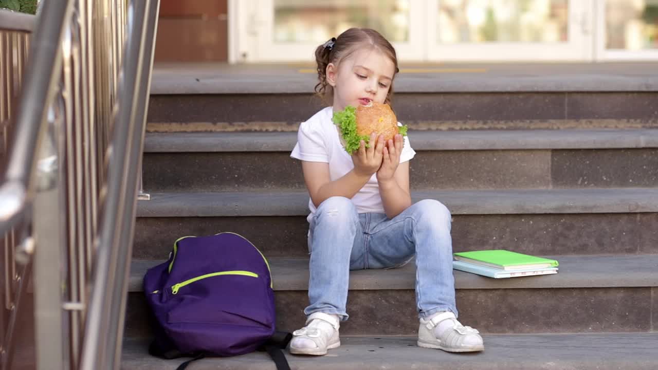 一个女学生在上学前吃午餐或汉堡小吃，这是一个回到学校或给学生喂食的概念，特写视频素材