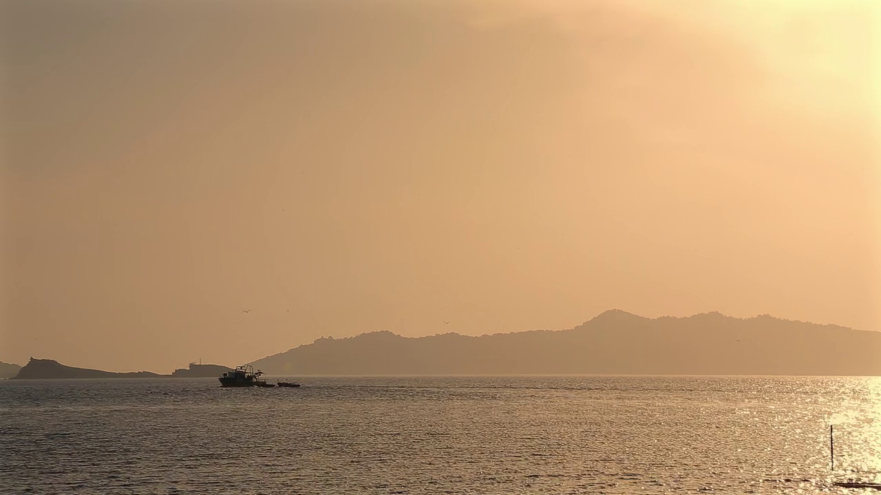 日落时的海景和山景。在山的背景下，一艘小渔船在航行。视频下载