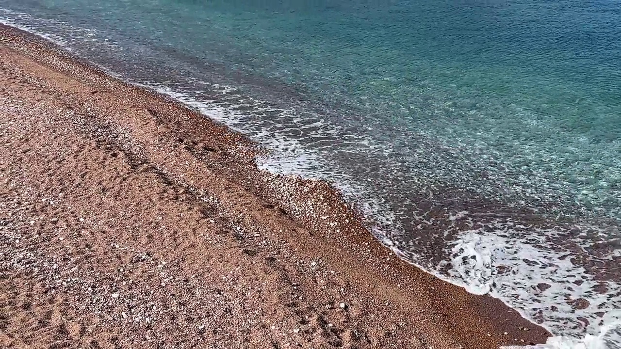 海水清澈，沙滩上有粉红色的鹅卵石和沙子。视频素材