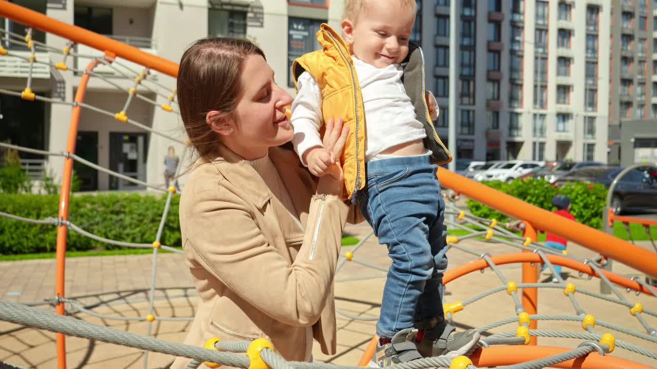 年轻的母亲扶着她的儿子在操场上保持平衡。孩子们在户外玩耍，孩子们在户外，暑假和假期视频素材