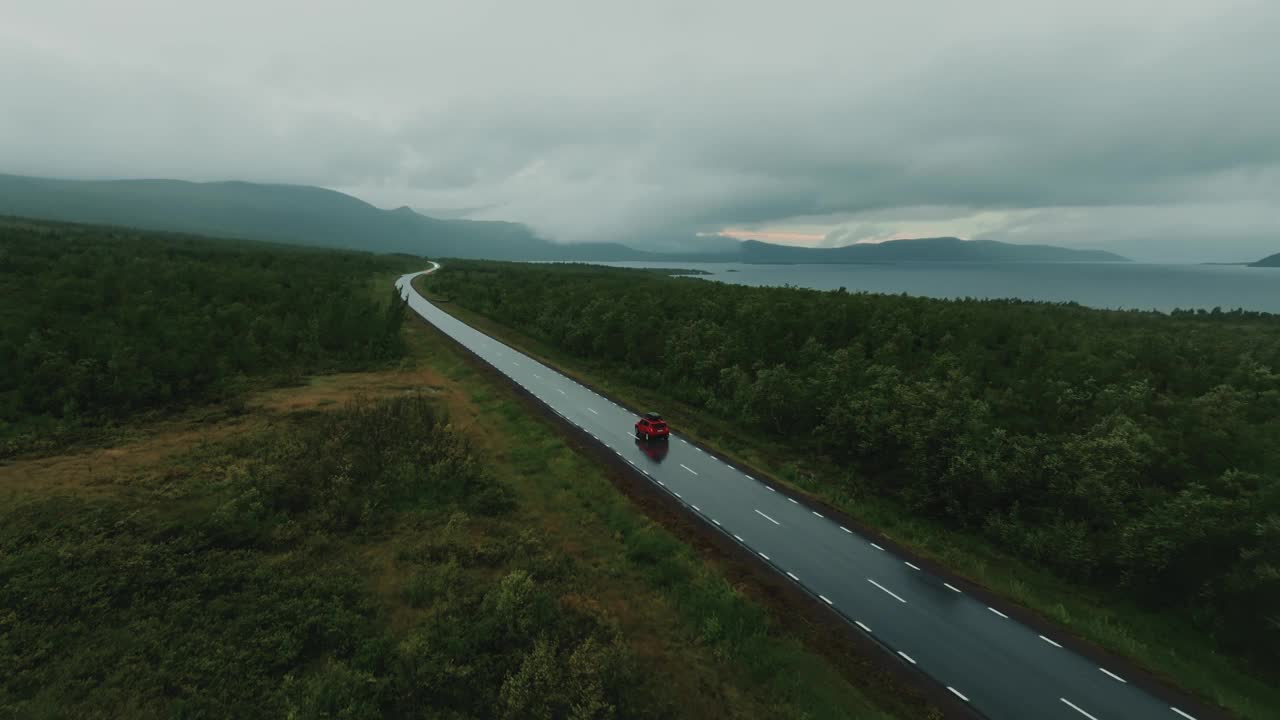 红色越野车独自驾驶，行驶在空旷的道路与史诗般的北欧景观在灰色的天。无人机航拍图。视频素材