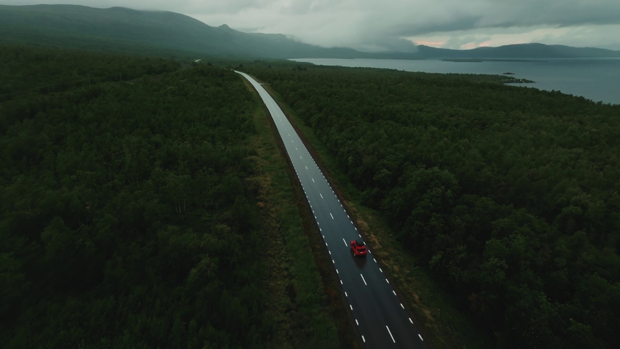 无人机飞过红色SUV，独自行驶在森林中央的道路上，背景是史诗般的北欧峡湾和湖泊视频素材