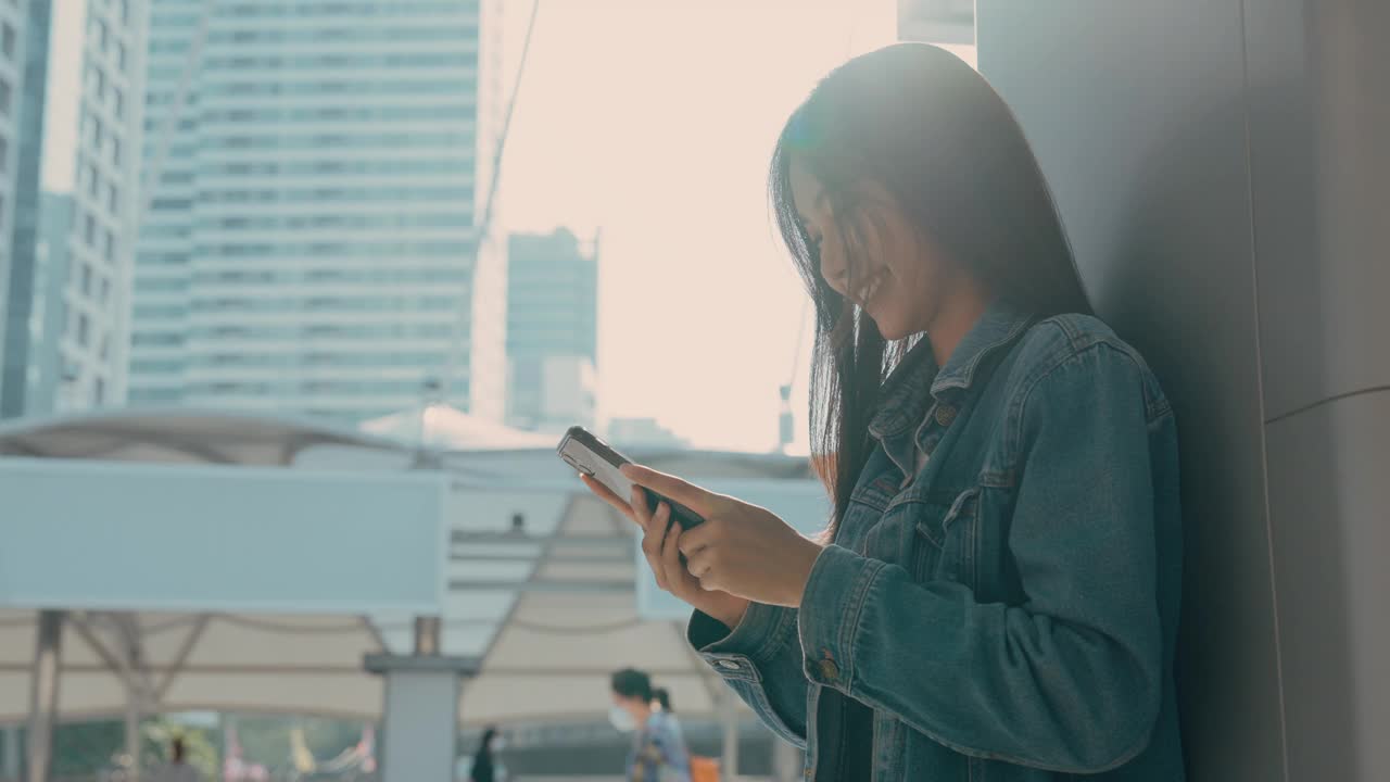 年轻的亚洲女子站在城市里，在街上使用手机视频素材