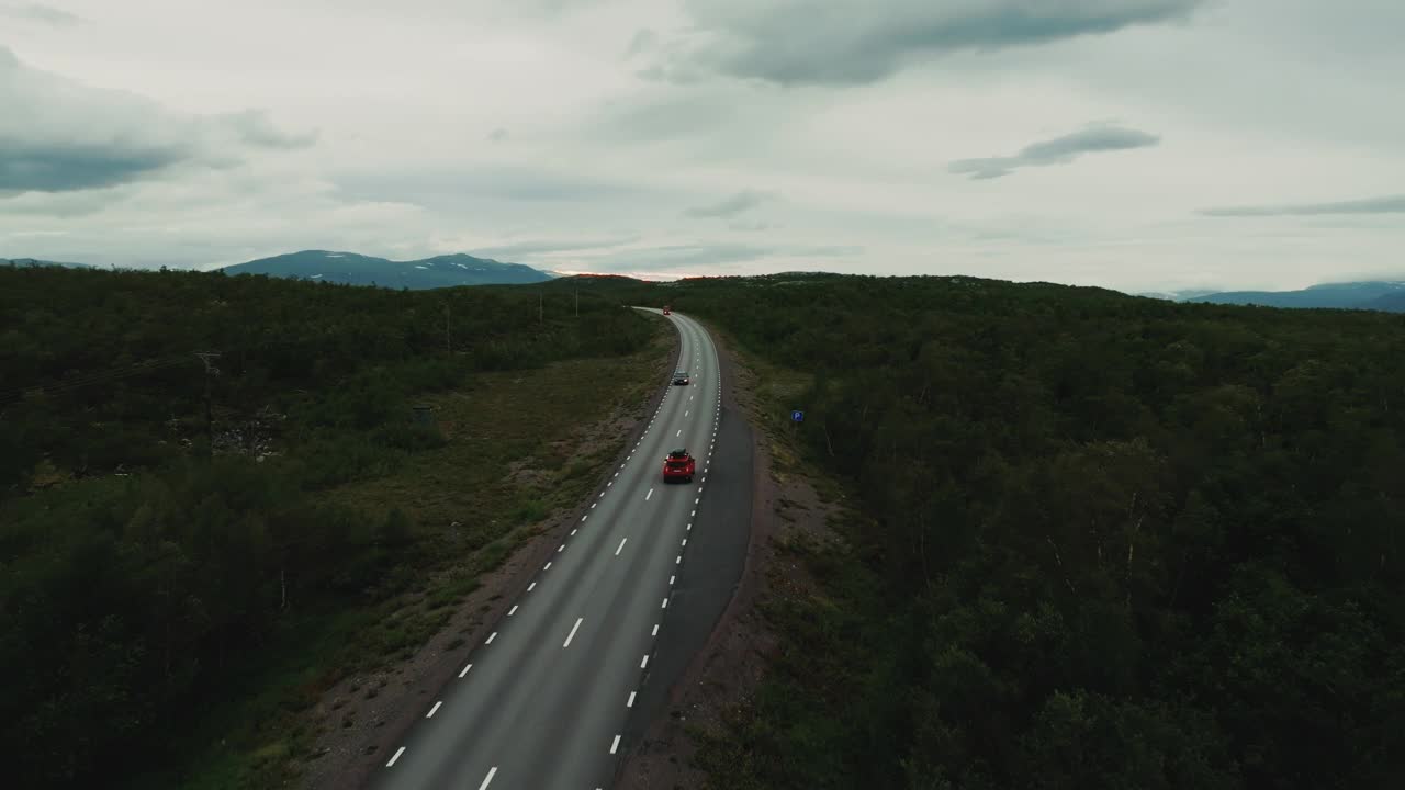 美丽的全景，一辆红色的汽车沿着乡间小路行驶，穿过树林，驶向群山视频素材