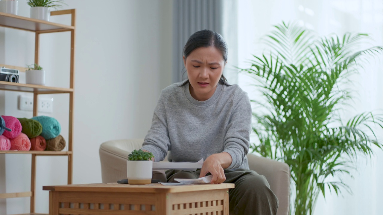 坐在扶手椅上的亚洲女性担心银行票据的账单支付问题，抵押贷款债务和生活成本。视频素材