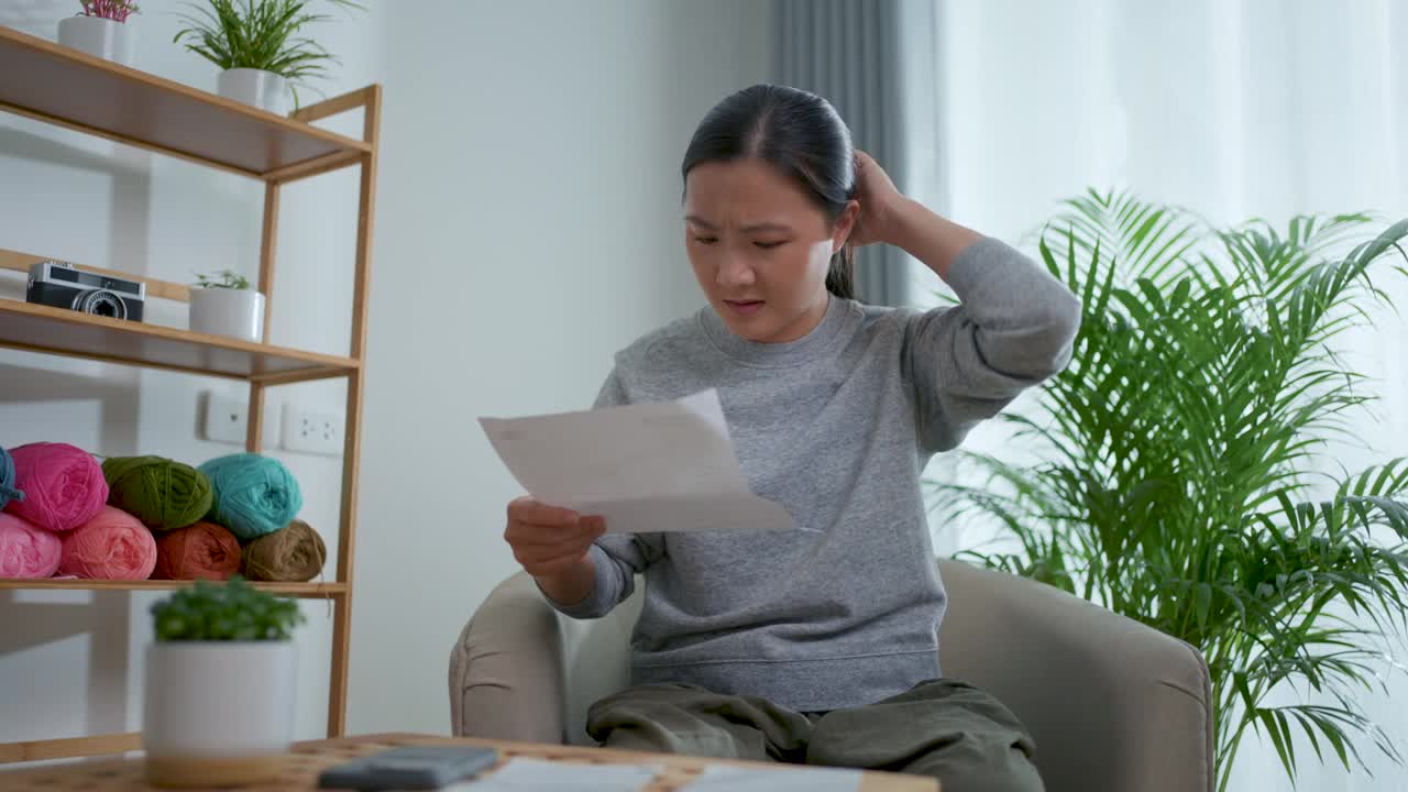 坐在扶手椅上的亚洲女性担心银行票据的账单支付问题，抵押贷款债务和生活成本。视频素材