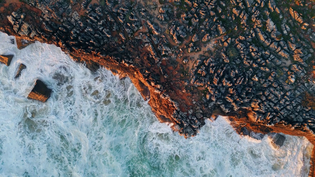 俯视图泡沫海水在海岸悬崖下飞溅。海浪泡沫海岸视频素材