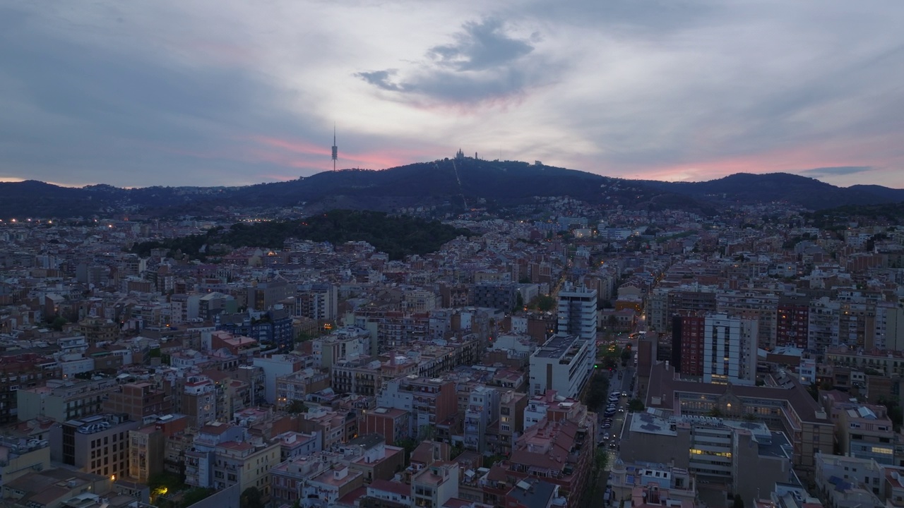 黄昏时大都市建筑物的航拍全景镜头。山上的电视塔和教堂映衬着色彩斑斓的黄昏天空。西班牙巴塞罗那视频素材