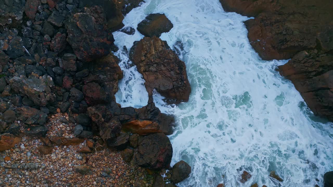 危险的岩石海岸与暴风雨的泡沫水撞击石头鸟瞰图。视频素材