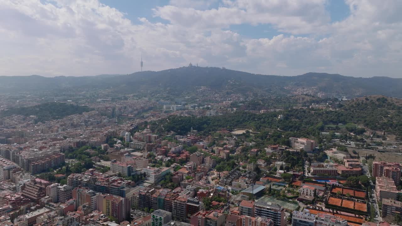 飞到大都市的上空。丘陵景观中的大城市鸟瞰图。高耸的电视塔和城市上方山上的耶稣圣心圣殿的剪影。西班牙巴塞罗那视频素材