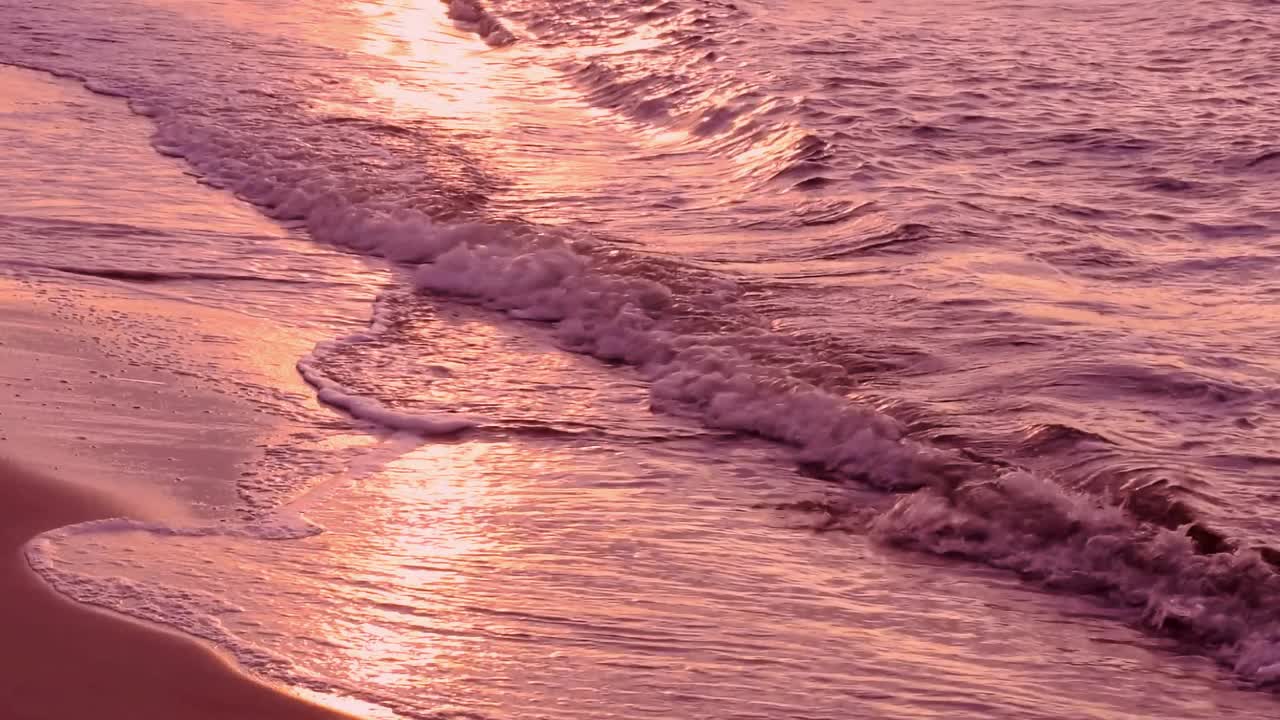 美丽的海浪与闪亮的反射彩色粉红色和紫色的夕阳光，由沙滩，阳光，海岸，波浪，户外，海景，风景，黄昏，慢动作，平静的场景，静态拍摄，特写，高清。422年ProRes总部视频素材