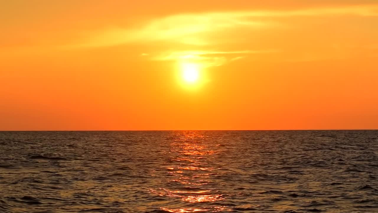 美丽的海浪反射着金黄色的夕阳。橙色天空上的彩云，平静的地平线场景视图，晴天，太阳，自然，阳光，阳光，户外，海景，早晨，静态，中景，慢镜头，高清。ProRes 422 HQ视频素材