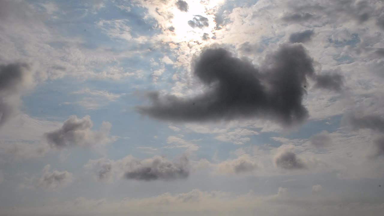 在晴朗的日子里，蓝色的天空中快速移动的云。黑色的小风暴云和白色的积云在天空中快速移动。自然背景自然背景。大气天气空中多云时程视频素材