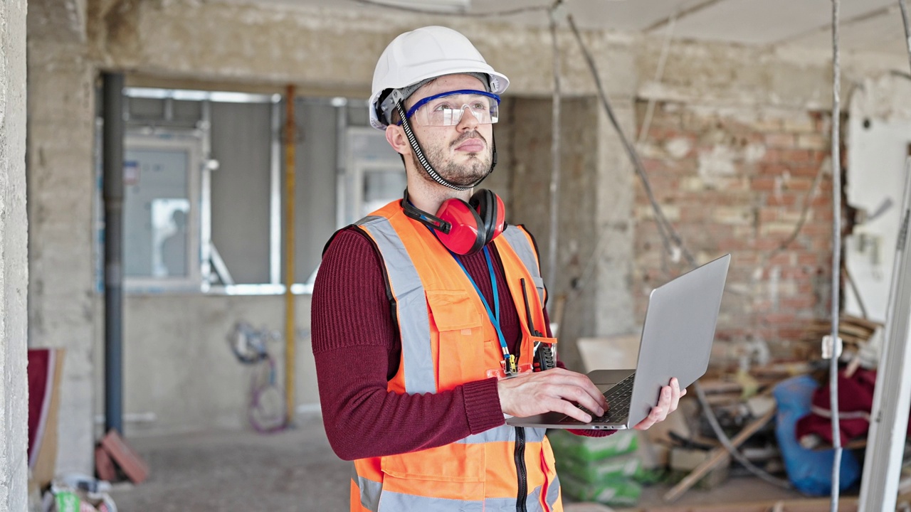 年轻的西班牙裔建筑工人用笔记本电脑环顾建筑工地视频素材