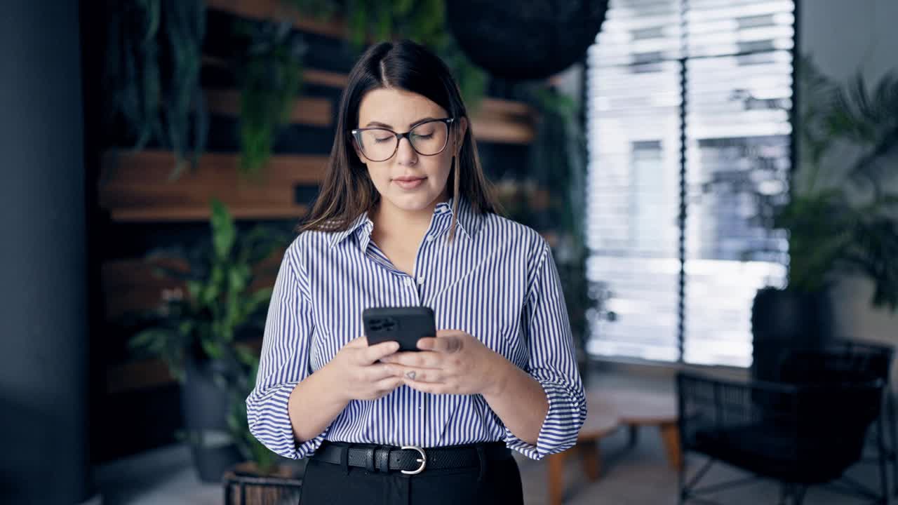 年轻美丽的西班牙女性在办公室用智能手机微笑着视频素材