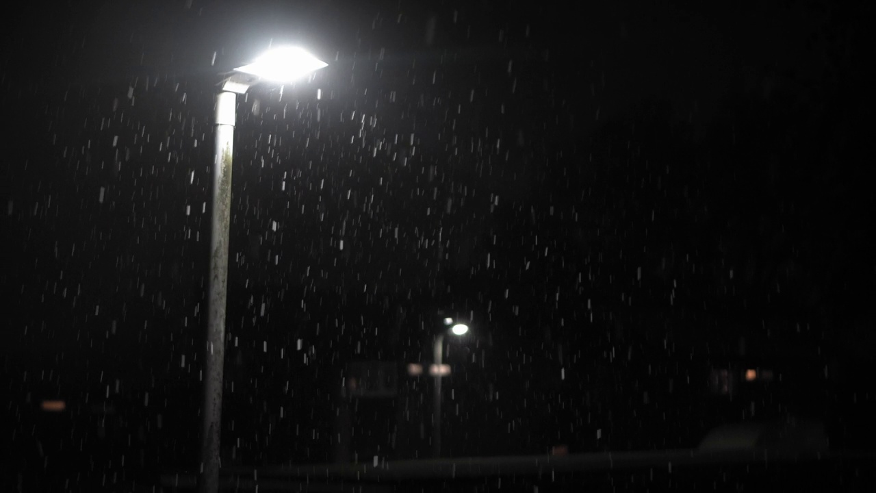 英国首次降雪叠加黑色背景。夜路路灯下的雪花-冬天，慢慢飘落的雪花效果。天气预报，异常，紧急概念视频素材