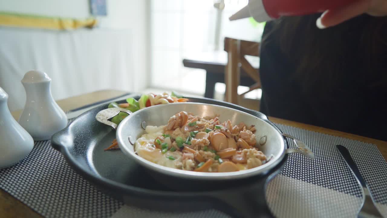 一名妇女正在往平底锅里浇鸡蛋酱和早餐配料视频素材